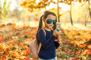 little girl with hourglass surrounded by autumn foliage