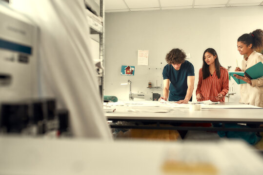 The joy of dressmaking. Young fashion designers working with sketches at studio, measuring and choosing fabric. Group of creative millennials working together