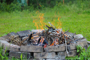 Burning bonfire in a brick fireplace on a background of green grass and blurred background