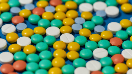 Different colorful pills scattered, lying randomly over blue background. Health care and treatment concept.