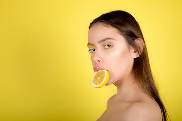 Beautiful young woman with lemon halves near eyes on yellow background