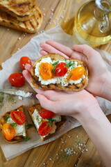 Children's hands hold a bruschetta with ricotta cheese and sun-dried tomatoes with Provencal herbs.
