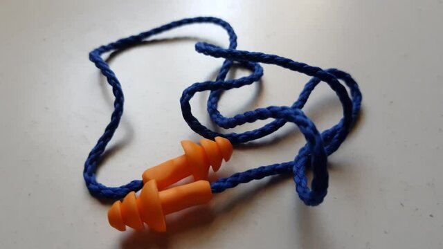 Orange earplugs with blue rope on a white table.