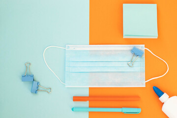 School and office supplies on bright blue (turquoise) and orange background: pen, clips, note paper,. Concept: back to school in new reality. Flatlay, top view.