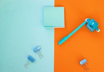 Set of school and office supplies on bright blue (turquoise) and orange background: pen, clips, note paper, toy robot. Concept: back to school. Flatlay, top view.