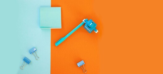 School and office supplies on bright blue (turquoise) and orange background: pen, clips, note paper, toy robot. Concept: back to school. Flatlay, top view, long banner.