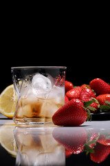 A glass of whiskey with ice on the background of strawberries