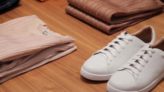 White sneakers, beige sweater, scarf, pullovers. Various clothes and shoes lie neatly on the table. Exposition of clothes and shoes.