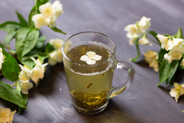 Glass cup with  jasmine  tea with blooming branches on black wooden background