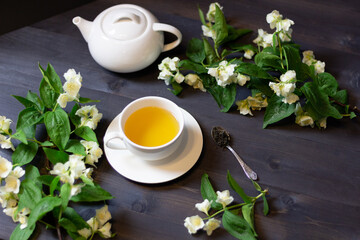 Cup of jasmine  tea with blooming branches, taepot and spoon on black wooden table