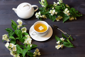 Cup of jasmine  tea with blooming branches, taepot and spoon on black wooden background