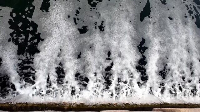 Top view of small waterfall in a pond as a sewage system to renew water. Waterfall with foam on water surface.