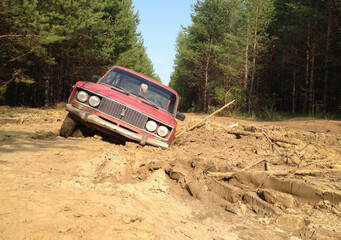 Obraz na płótnie Canvas A red passenger car stuck deep in the mud on a forest road.