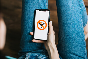 Young woman holding mobile phone with no internet or wifi sign at home.