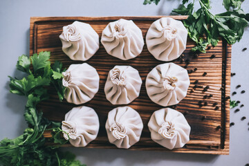 Khinkali dumplings pastry dish on a wooden board, decorated with parsley and peas of black pepper. top view