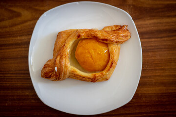 Peach puff bun on a white plate on a wooden table.