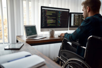 I can work with any code. Concentrated male web developer in a wheelchair writing program code on...