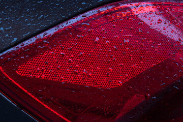 Close-up of the red taillight of a brown modern car with raindrops