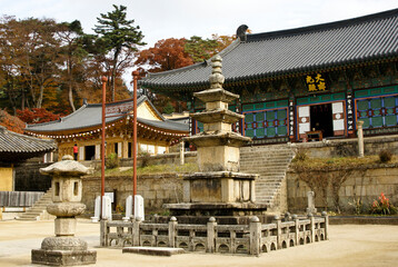 Obraz premium A stone lantern and three-tier pagoda in the upper courtyard at Haeinsa (Haein-sa) Buddhist temple in South Korea are surrounded by old buildings and autumn colors