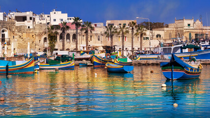 Fototapeta na wymiar Marsaxlokk village and traditional boats reflected in the sea at sunset on the harbour of Malta