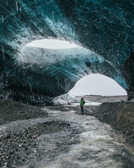 Blue crystal ice cave and human figure beneath the glacier in Iceland. Traveler in ice cave, man standing underground inside of a glacier, climate specific, Vatnajokull National Park.