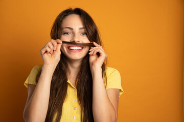 laughing young woman who makes a mustache with a lock of her hair on an orange background