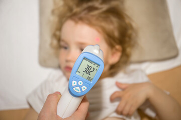 Temperature measurement by a laser thermometer. Little curly redhead girl. Child disease concept