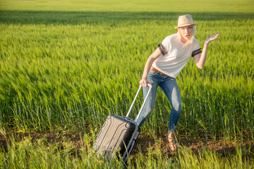 Sexy blonde girl in a hat with a suitcase on a background of green field, with space for text