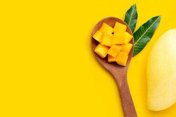 Sliced ripe mango cubes on wooden spoon on yellow background.