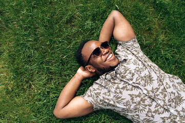 Portrait of a handsome young smiling african american man whos resting  on a grass in nature during...