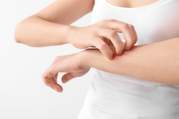 Young woman scratching her skin on light background