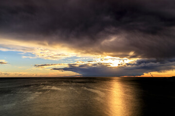 Sunrise over the sea with sun rays passing through dark storm clouds
