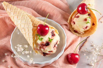 Traditional waffle cones with ice cream and cherry fruits on marble stone surface
