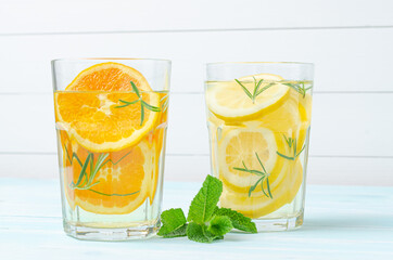 Preparation of the lemonade drink and orange juice Lemonade in the jug and lemons with rosemary on the table outdoor.