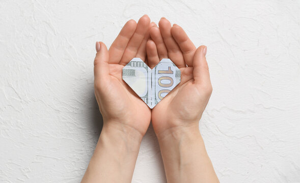 Female hands with origami heart made of dollar banknote on white background