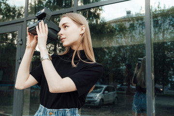A beautiful stylish blonde walks with a film camera нipster casual 
against the background of a skyscraper