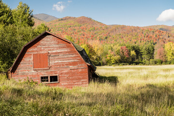 Obraz premium Old red barn in a field with Autumn colors in mountains in the background.