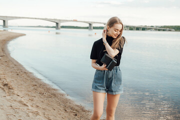 A beautiful stylish blonde walks with a  retro film camera нipster casual
against the sea rivers