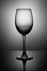 Transparent wine glass stands on black glossy glass, back spot illumination