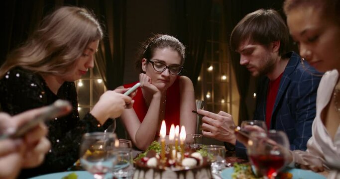 Group of bored multiethnic friends at a birthday party. Sad caucasian girl looking at people staring at their phones and surfing internet - real people concept 4k footage