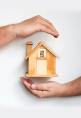 detail of male hands surrounding a small wooden house on white background