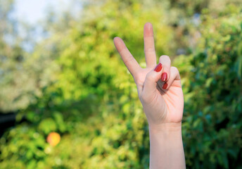 female left hand with red nails doing victory and peace gesture with nature background