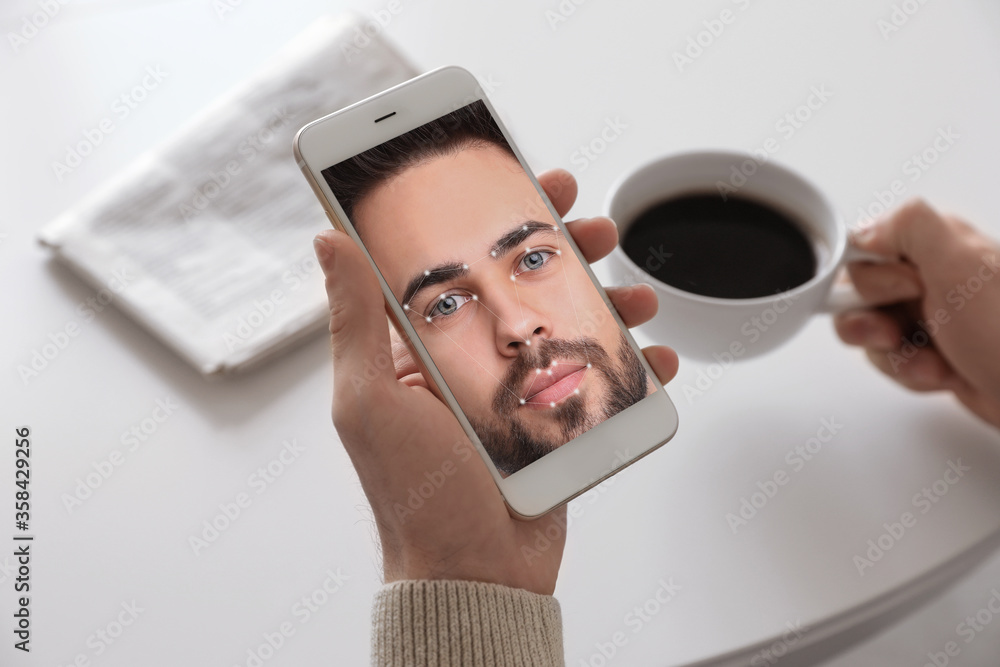 Poster man using smartphone with facial recognition system at table, closeup. biometric verification