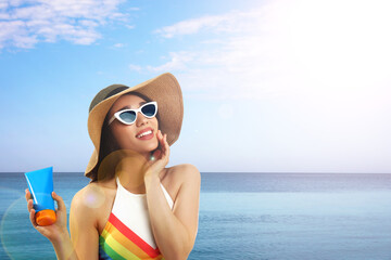 Young woman with sun protection cream near sea, space for text