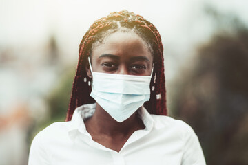 An outdoor portrait of a young African female with chestnut braids and in a virus protective mask...