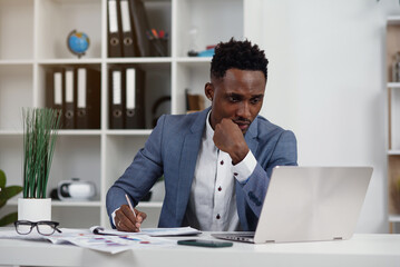 Businessman with laptop. Young African businessman is typing something on laptop in his office.
