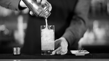 Bartender shaking cocktail in cocktail shaker at bar black and white