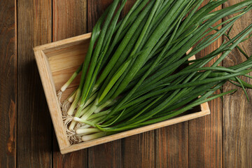 Fresh green spring onions in crate on wooden table, top view
