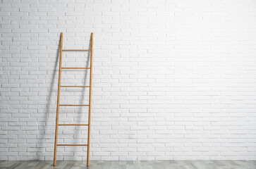 Modern wooden ladder near white brick wall. Space for text