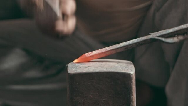 Hands of a rural blacksmith hammering a metal rod on an anvil